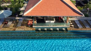 An aerial view of a swimming pool with a bar area, lounge chairs, and a red-roofed building. - Elysium Suite (Siem Reap)