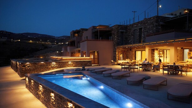 Una piscina con sillas de descanso y una zona de bar, rodeada de muros de piedra y arquitectura moderna.