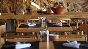 Un restaurante con mesas y sillas de madera, un fondo de pared de piedra y un tazón de frutas sobre la mesa.