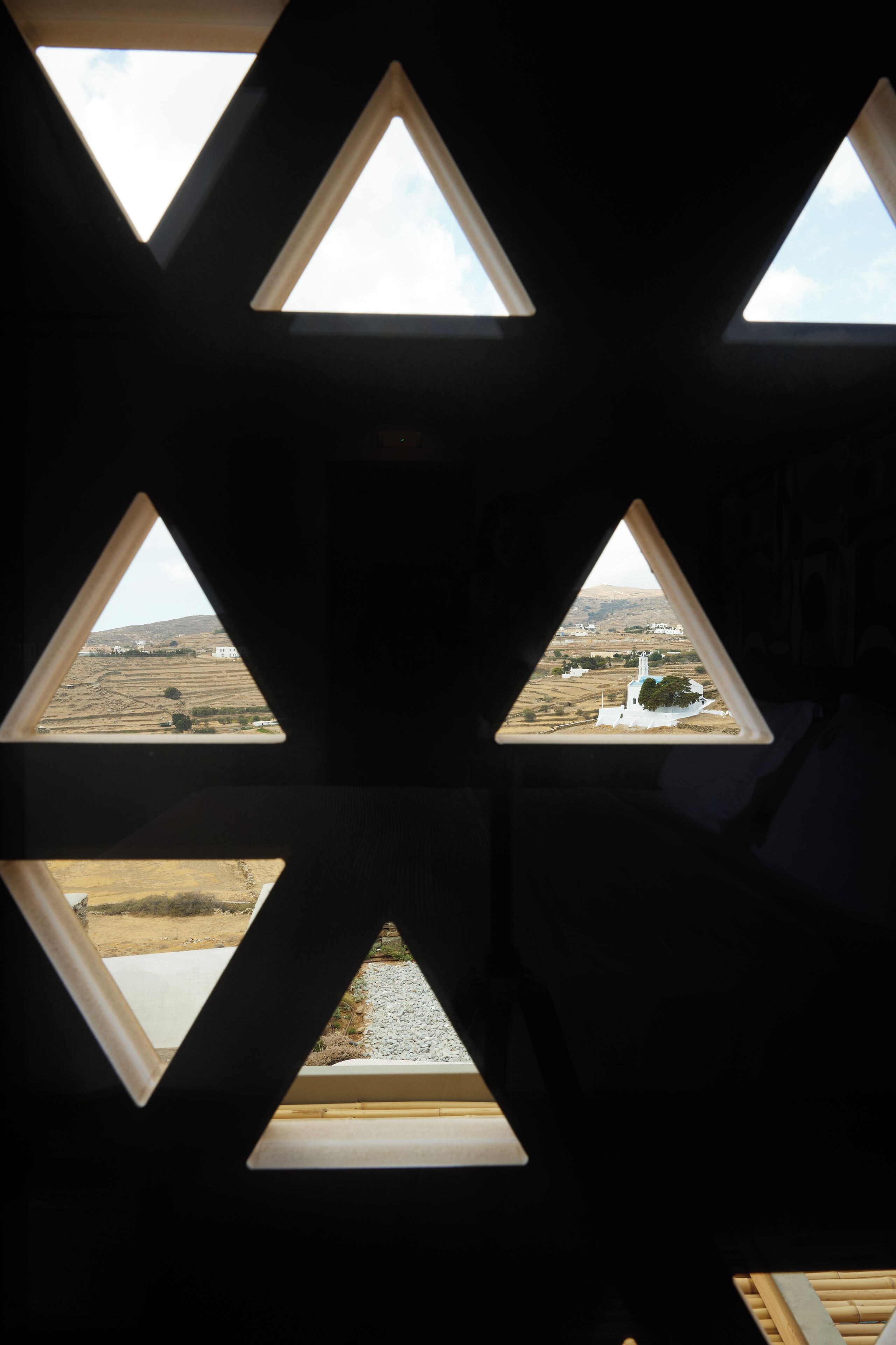 A room with triangular windows offering views of a landscape with a white building and a body of water.