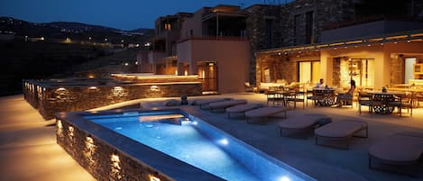 A swimming pool with lounge chairs and a bar area, surrounded by stone walls and modern architecture.