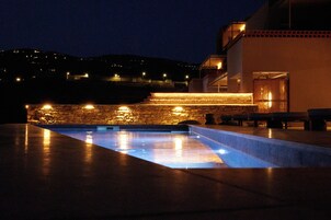 Una piscina con paredes de piedra y una zona de bancos de piedra, rodeada por un edificio con balcón.