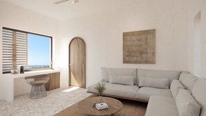 A modern living room with a large window, a wooden door, a beige sofa, a round wooden coffee table, and a woven rug. - Sun Aeriko (Tinos)