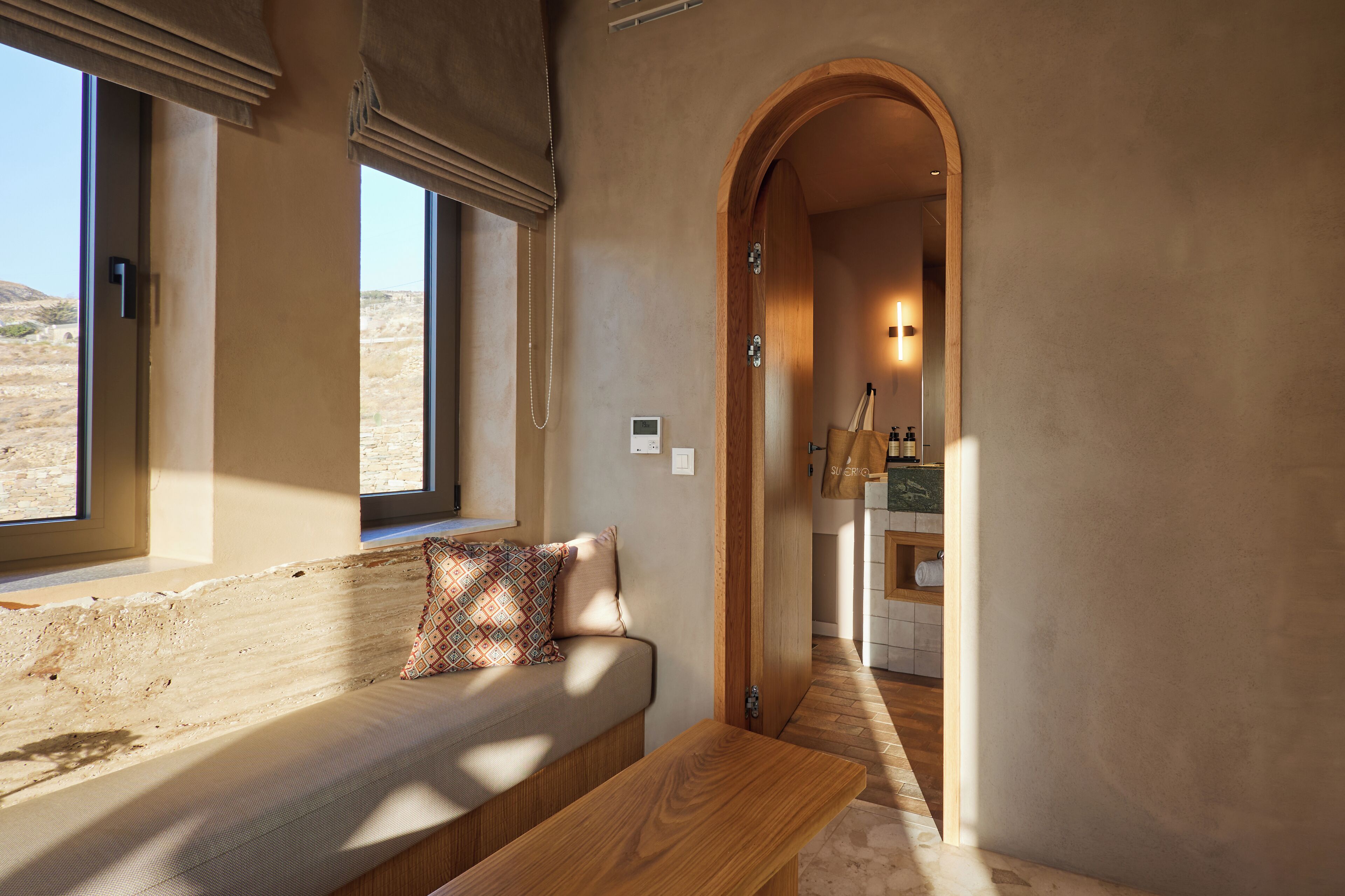 Una habitación con un banco empotrado, una ventana y un arco que conduce a una zona de cocina.