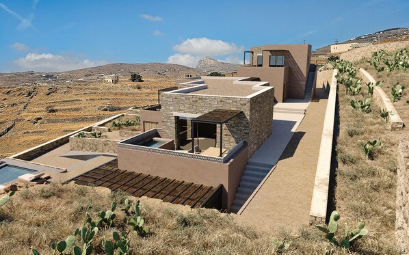 A modern villa with a stone facade, a rooftop pool, and a view of the surrounding landscape. - Sun Aeriko (Tinos)