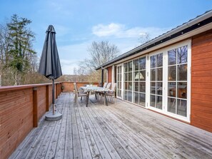 Une terrasse en bois avec une table et des chaises, un parasol et une porte vitrée donnant sur une pièce.