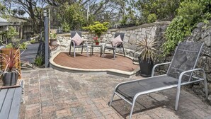Een terras met houten terras, stenen muur en buitenmeubilair, waaronder twee stoelen en een tafel.
