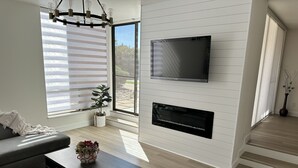 Un saló modern amb televisió de pantalla plana, una llar de foc i una finestra gran amb persianes.