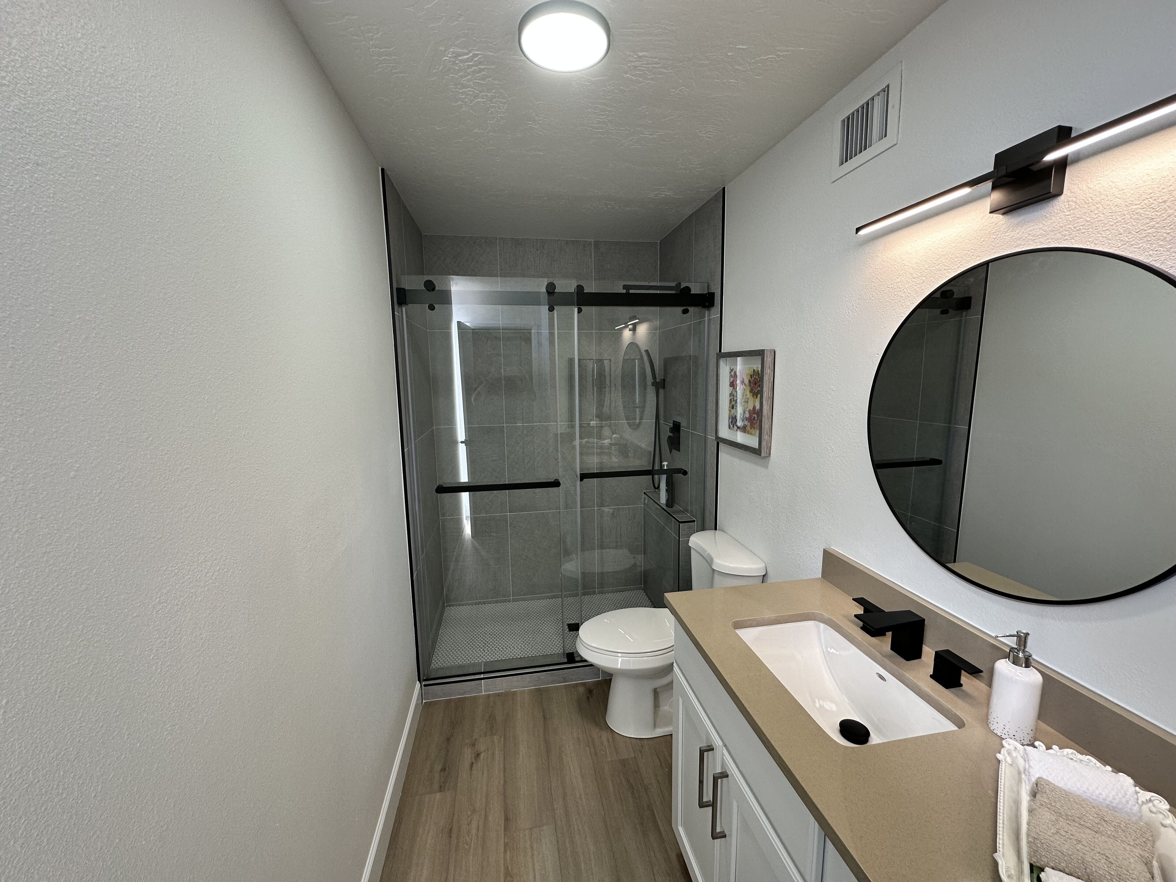 A modern bathroom with a glass-enclosed shower, a white toilet, a beige vanity with a large mirror, and a sink.