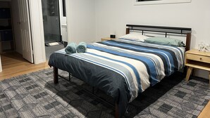 Une chambre à coucher comprenant un lit, une table de chevet, une fenêtre et une porte donnant sur une salle de bain.