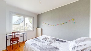 A bedroom with a bed, a desk, and a chair. There is a window with a view of a building outside. - 3 bedroom stunning home in Lanvaudan (Lanvaudan)
