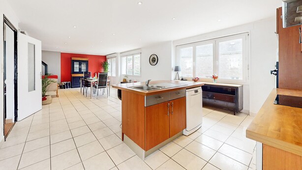 A modern kitchen with a central island, a dining area with a red accent wall, and a view of the street through large windows. - 3 bedroom stunning home in Lanvaudan (Lanvaudan)