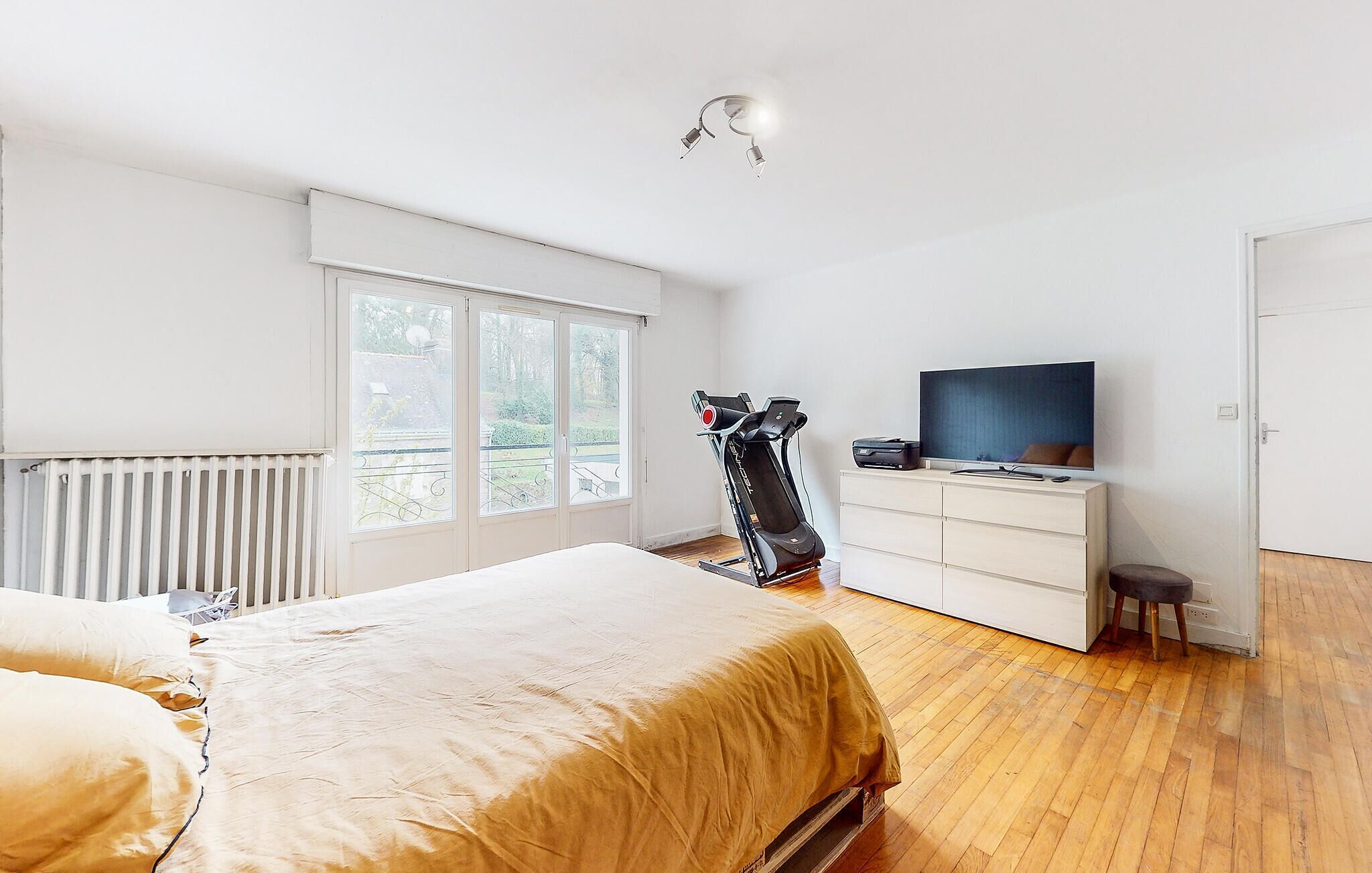 A bedroom with a bed, a treadmill, a TV, and a dresser.