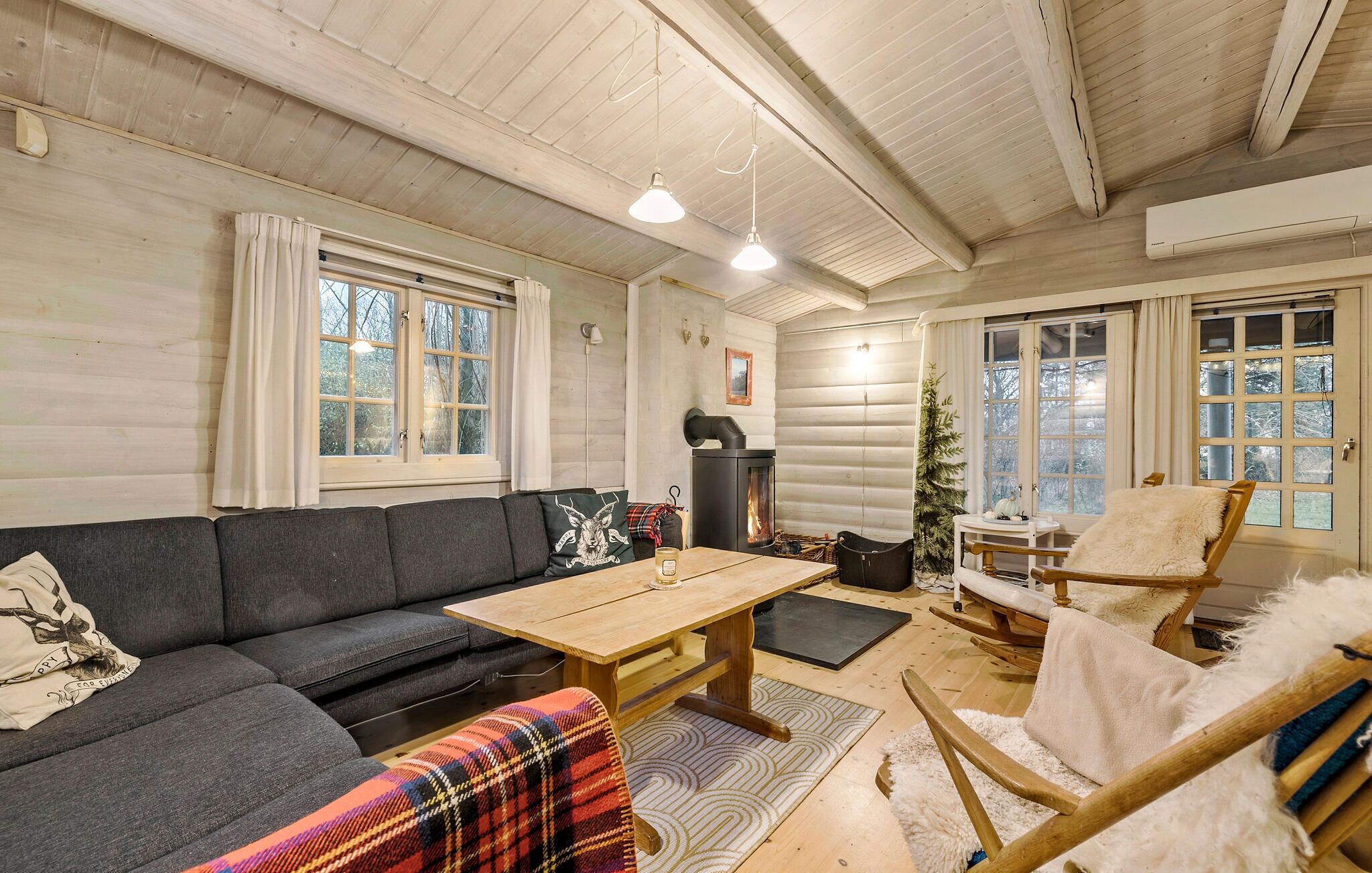 A cozy log cabin interior with a sofa, a wooden table, a rocking chair, and a fireplace.