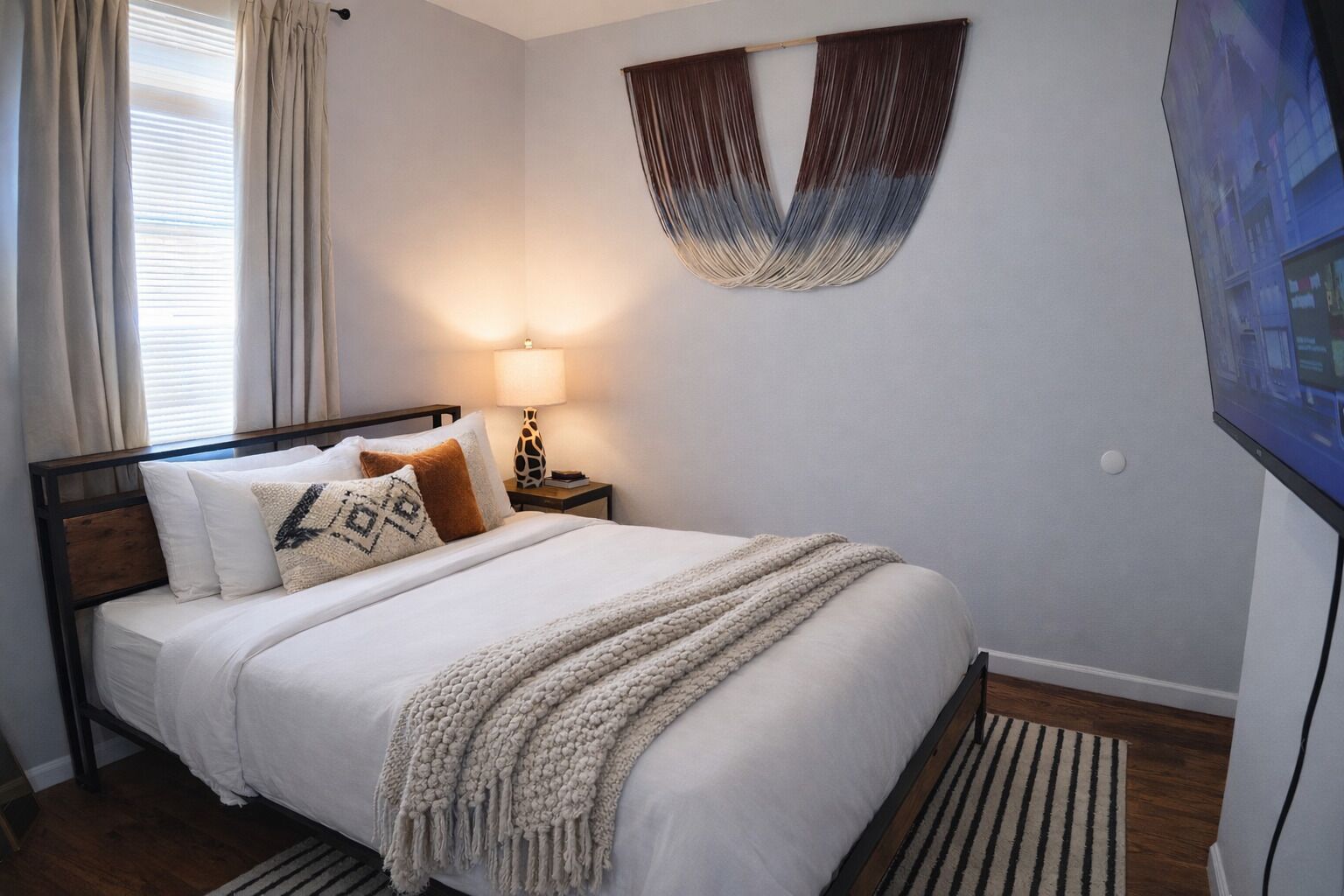 Un lit bien fait, avec une tête de lit, une lampe de chevet et une œuvre d’art accrochée au mur.