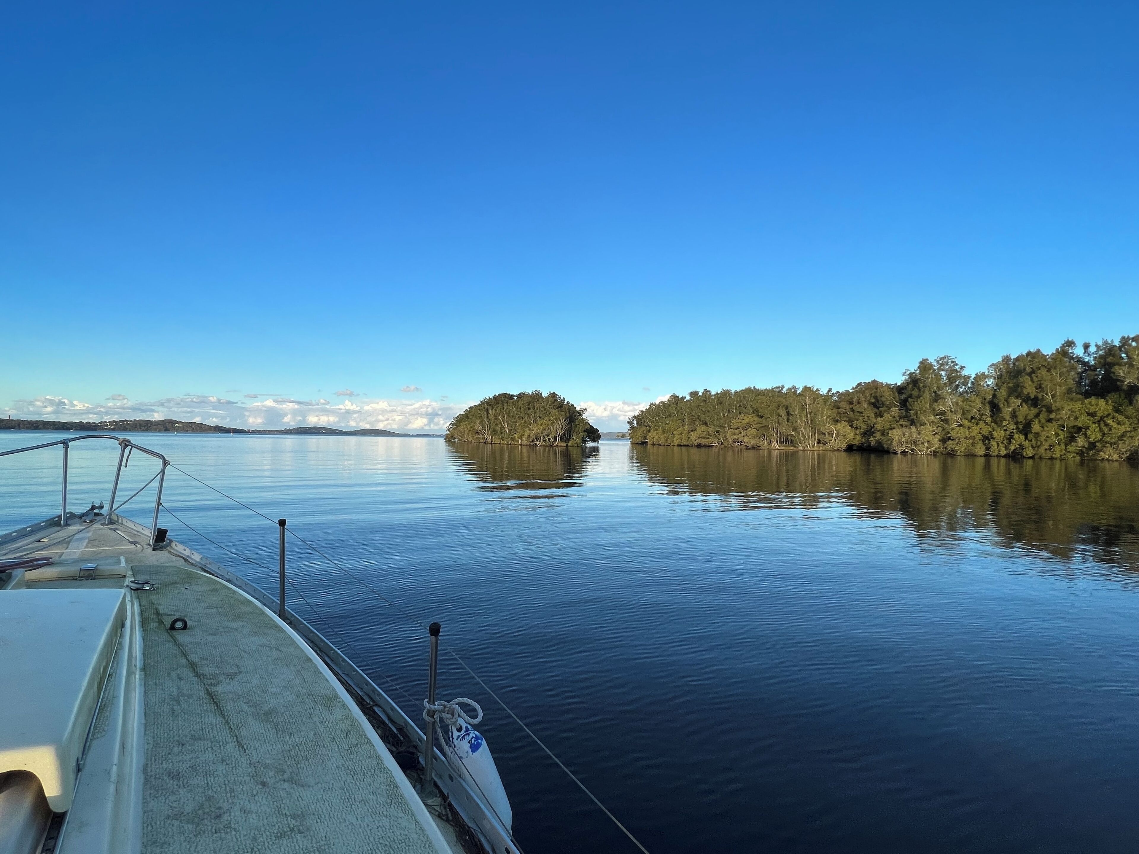 Een kalm meer met een boot op de voorgrond en een bebost eiland in de verte.