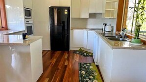 A modern kitchen with white cabinets, a black refrigerator, and a wooden floor.