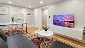 Ein modernes Wohnzimmer mit Flachbildfernseher, einem Essbereich mit Glastisch und Stühlen sowie einem Sofa.