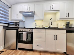 A modern kitchen with white cabinets, a built-in oven, a microwave, and a coffee machine.