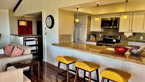 A modern kitchen with a central island, bar stools, and a dining area with a sofa and chairs.