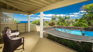 A covered outdoor area with a pool, wicker furniture, and a view of the ocean.