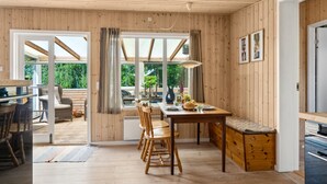 A wooden cabin with a dining area, kitchen, and a large window offering a view of greenery.