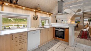 Una cocina moderna con armarios de madera, lavavajillas y un amplio ventanal con vistas a un césped.