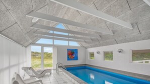 Una piscina interior con vista despejada al exterior, techo con diseño geométrico y un cuadro abstracto colorido en la pared.
