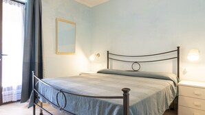 A bedroom with a metal bed frame, a bedside table, a nightstand, and a wall-mounted lamp. - Gardenia Apartment, centrally located, perfect for those who want to forget the car, with outdoor sp (Marina di Campo)