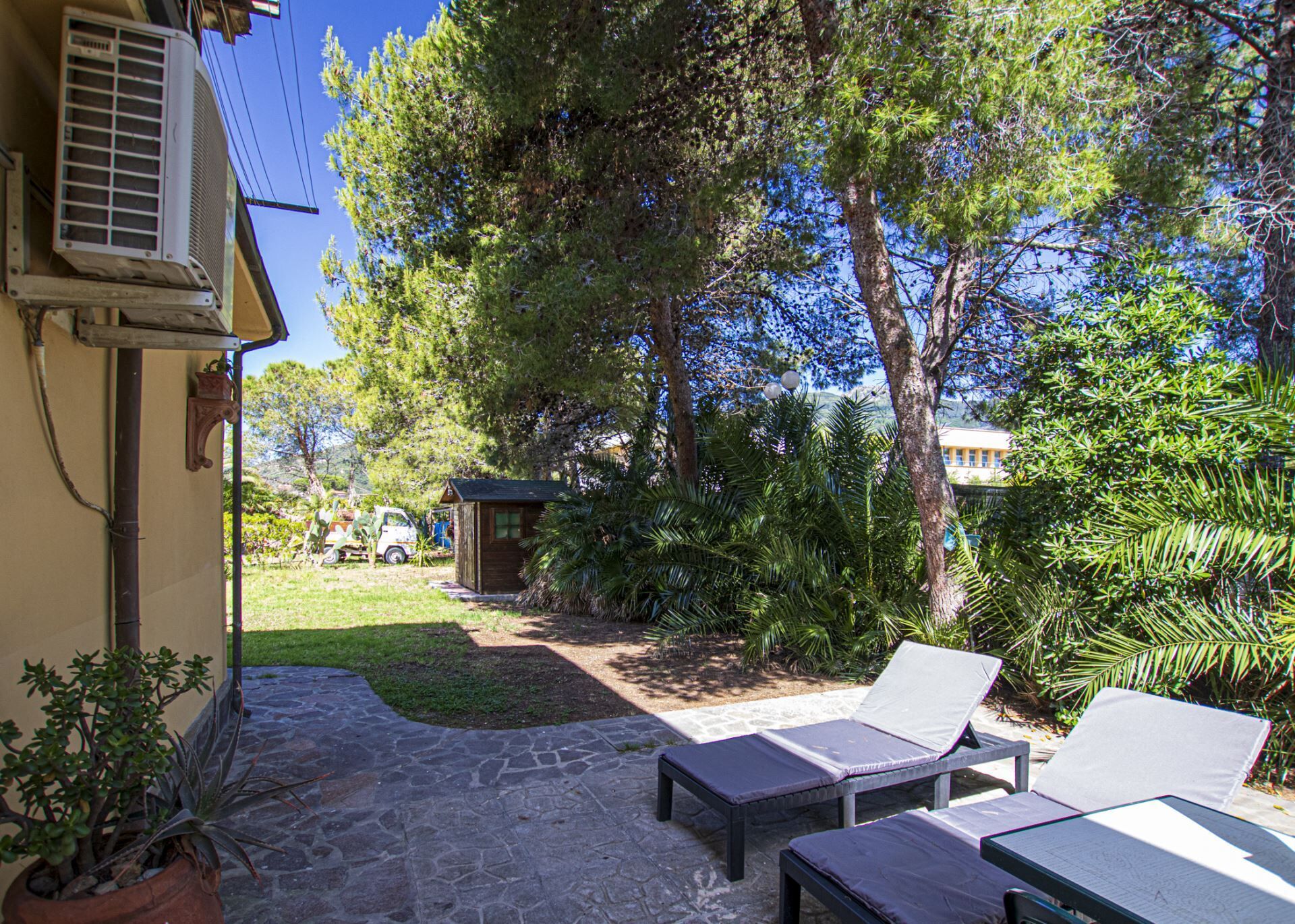 A patio with stone flooring, lounge chairs, and a small wooden structure.