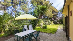 An outdoor patio with a table and chairs, surrounded by lush greenery and a yellow building. - Gardenia Apartment, centrally located, perfect for those who want to forget the car, with outdoor sp (Marina di Campo)