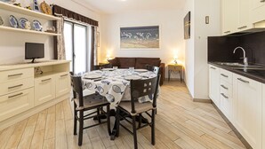 A compact kitchen with white cabinets, a dining table with chairs, a small TV, and a painting on the wall. - Gardenia Apartment, centrally located, perfect for those who want to forget the car, with outdoor sp (Marina di Campo)