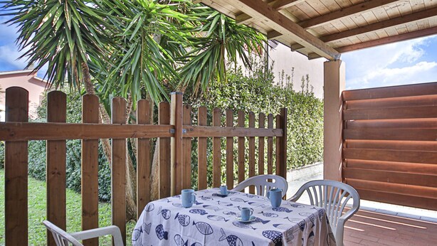 Une terrasse couverte avec une table dressée pour deux personnes, entourée de chaises en bois, sous une pergola en bois.