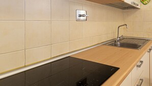 Une cuisine moderne dotée d’une plaque de cuisson à induction noire, d’un évier en acier inoxydable et de meubles de rangement en bois.