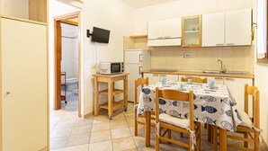 Une cuisine compacte avec un coin repas, un micro-ondes posé sur une petite table et un téléviseur fixé au mur.