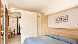 Une chambre à coucher comprenant un lit, une tête de lit en bois, un climatiseur fixé au mur, une petite table avec des chaises et une porte donnant sur une autre pièce.