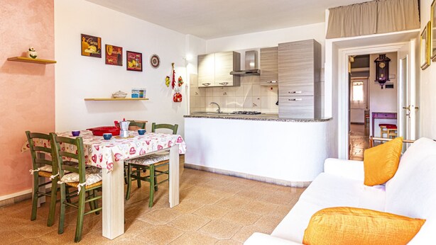 Un espacio habitable compacto con zona de comedor, kitchenette y un sofá con cojín.