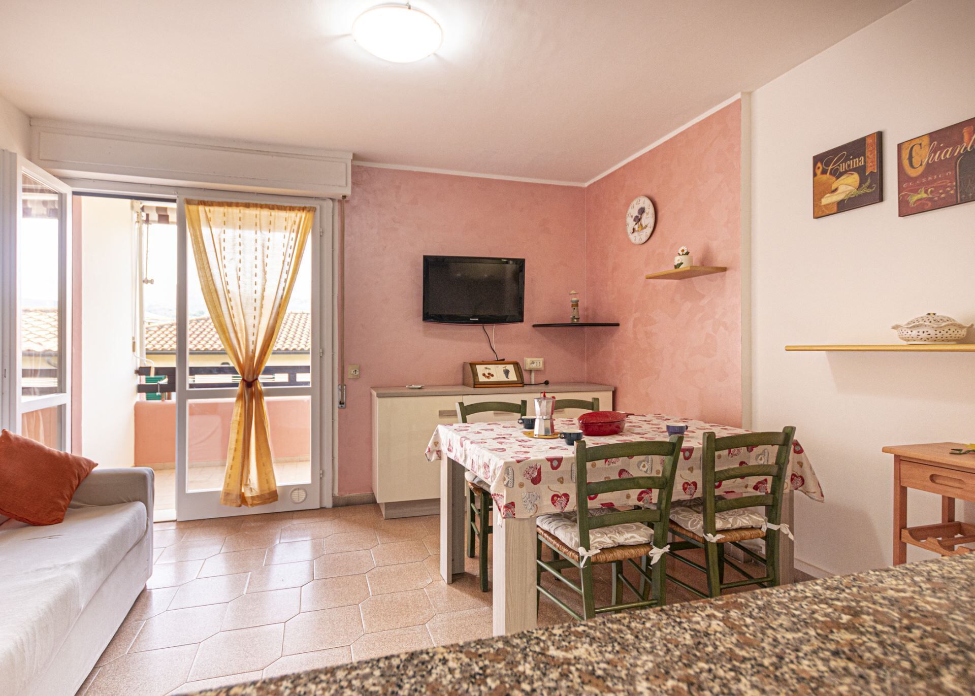A cozy living room with a sofa, a dining table with chairs, a TV, and a kitchen area with a microwave and a coffee maker.