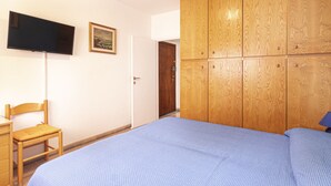 Un dormitorio con cama, un armario de madera, un televisor en la pared y una silla.