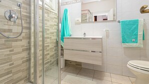 Un baño con cabina de ducha de vidrio, un lavamanos blanco, un espejo y un inodoro.