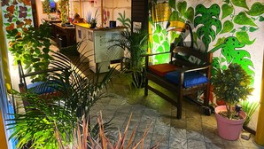 Un espace intérieur accueillant, avec un bureau en bois, un banc doté d’un coussin et diverses plantes en pot.