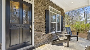 A stone exterior with a dark front door and windows, outdoor seating with chairs and a table, and a stone patio. - Luxury Home - ATL - No Cleaning Fee! (Austell)