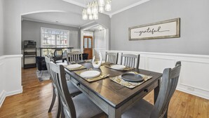 A dining room with a wooden table set for six, white walls, and a 'grateful' sign on the wall. - Luxury Home - ATL - No Cleaning Fee! (Austell)