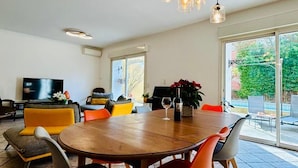 Un vaste espace de vie comprenant une table à manger ronde en bois, des chaises modernes et une grande fenêtre donnant sur l’extérieur.
