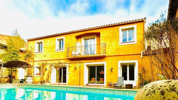 Une villa jaune avec une piscine, un patio couvert et un grand pot en céramique.