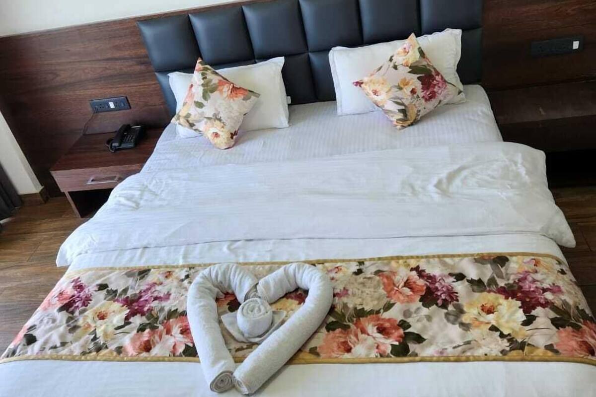 A neatly made bed with floral bedding, a heart-shaped towel, and a wooden headboard.