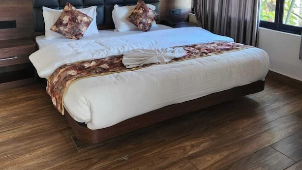 Une chambre spacieuse avec un grand lit, une tête de lit en bois et une vue sur la verdure par la fenêtre.
