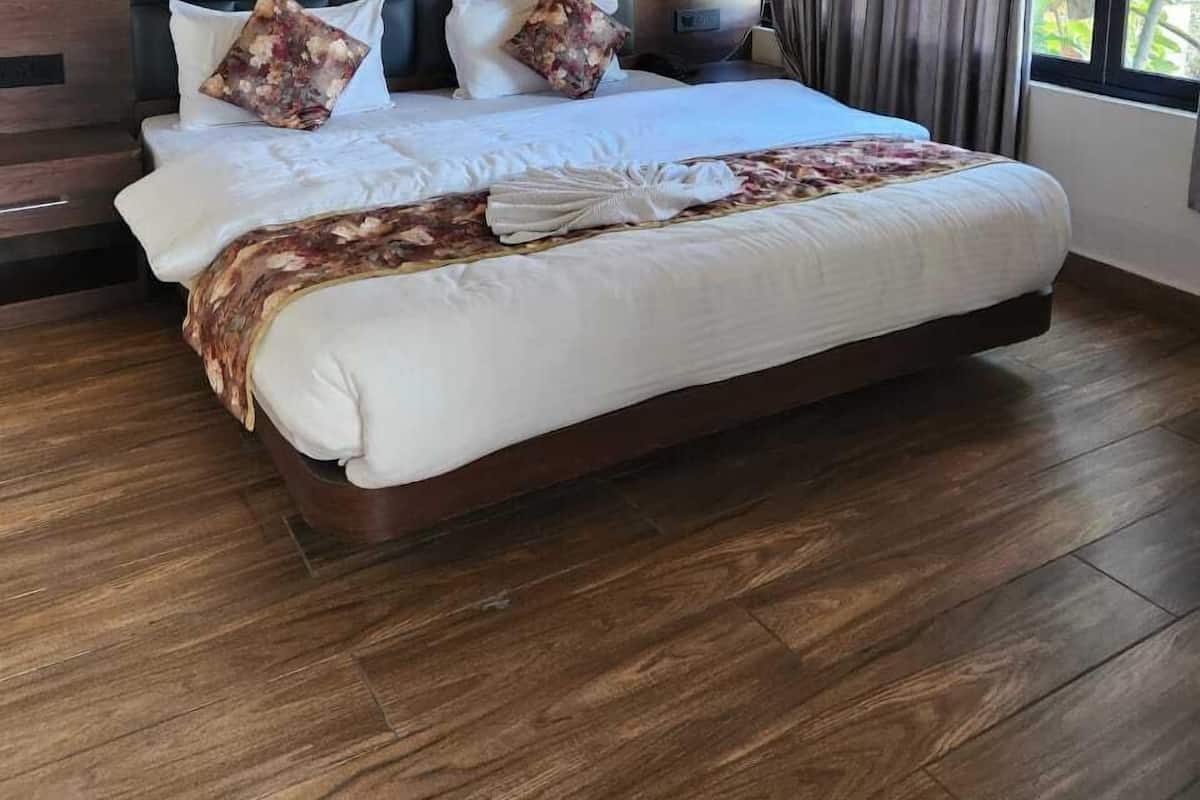 A spacious bedroom with a large bed, wooden headboard, and a view of greenery through the window.