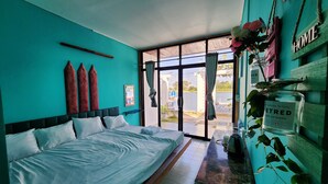 A bedroom with a large bed, a view of the outdoors through a glass door, and a shelf with decorative items. - Port Ville Resort (Kampot)