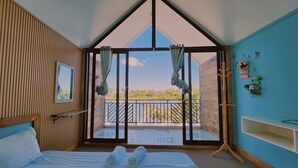 A bedroom with a large window, a bed, a wooden headboard, a bedside table, and a view of a balcony. - Port Ville Resort (Kampot)